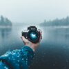 person holding a Nikon camera in one hand against a misty lake background