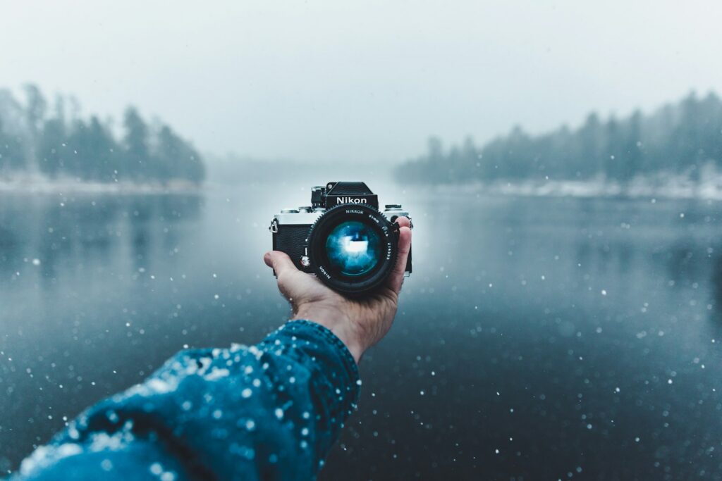 person holding a Nikon camera in one hand against a misty lake background