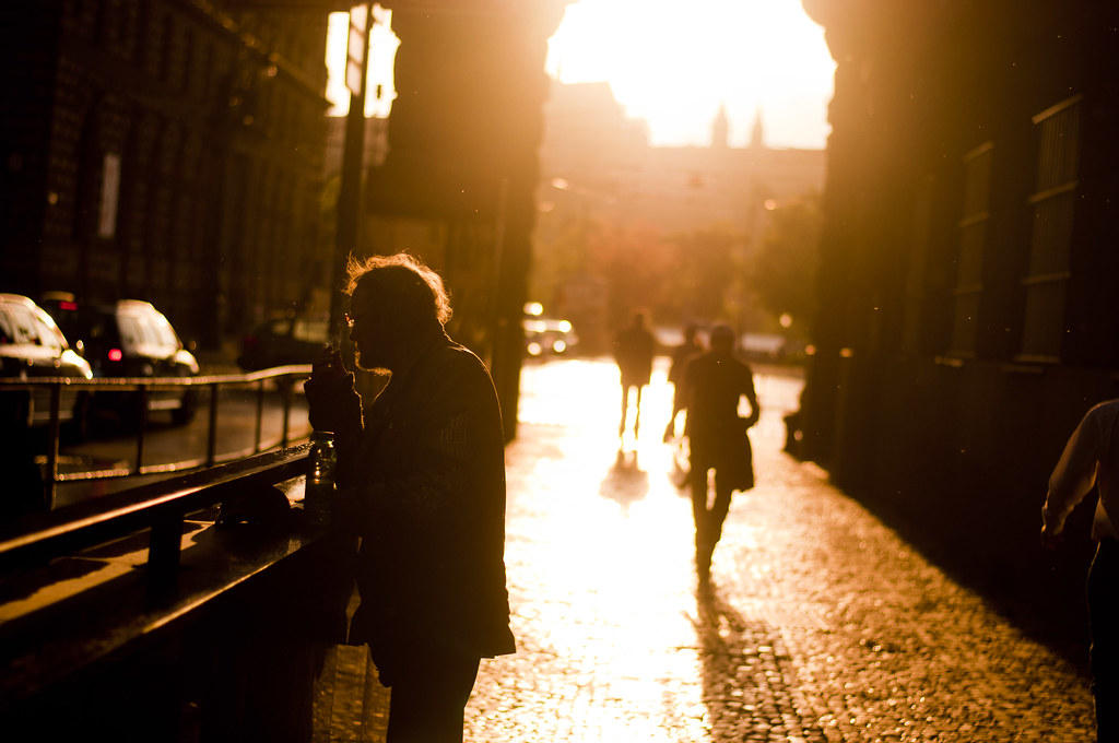 silhouetted figure with a camera on a city street backlit by golden hour sun, with pedestrians in the background