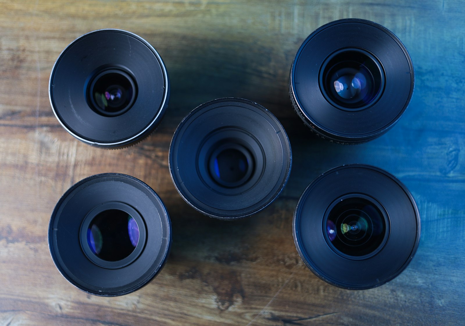 five camera lenses standing upright on a wooden table
